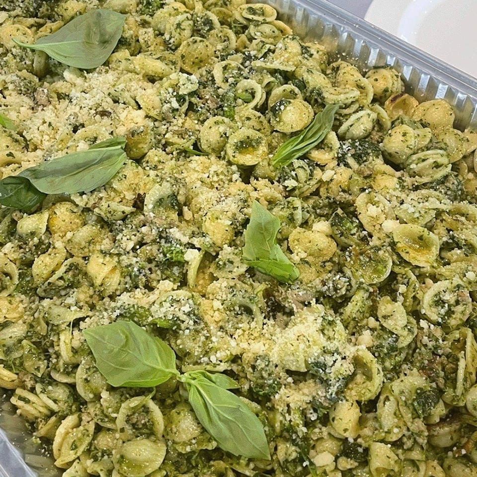 Tray of orecchiette pasta tossed with green pesto, breadcrumbs, grated cheese, and fresh basil leaves.