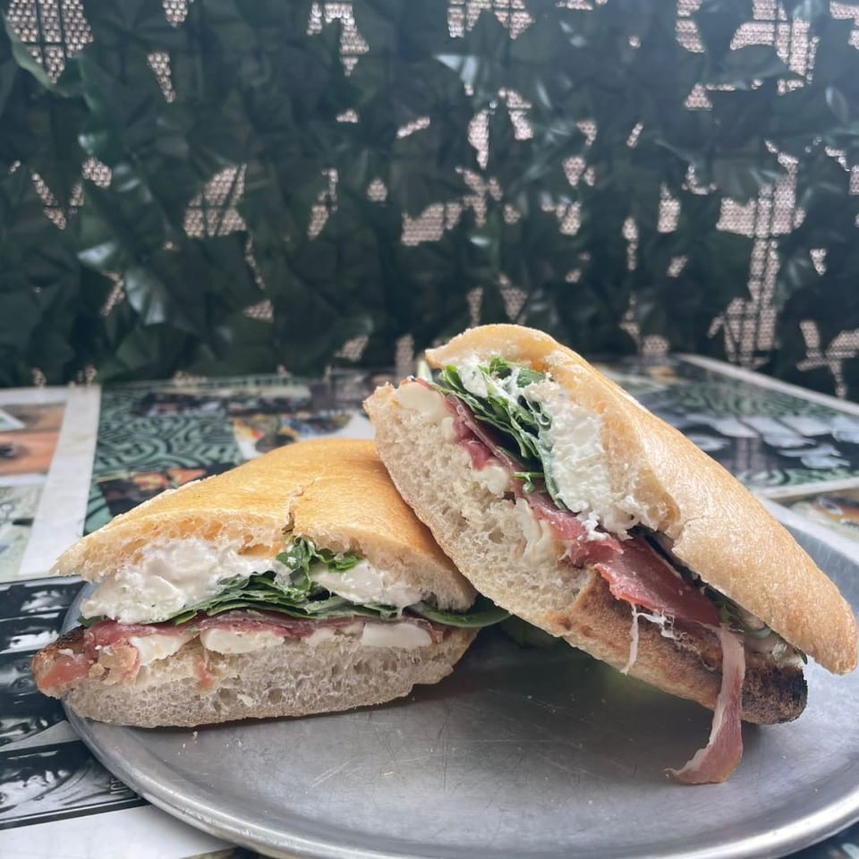 Two baguette sandwiches filled with sliced meat, creamy cheese, and leafy greens on a metal plate.