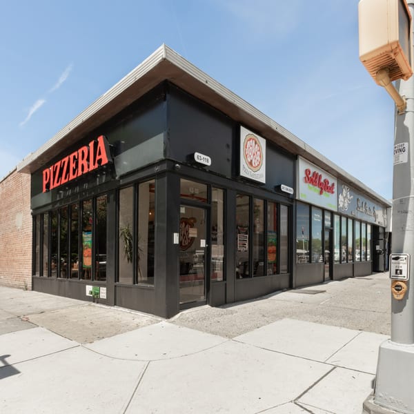 Exterior of a black pizzeria building with large windows and a red "PIZZERIA" sign on a sunny day.