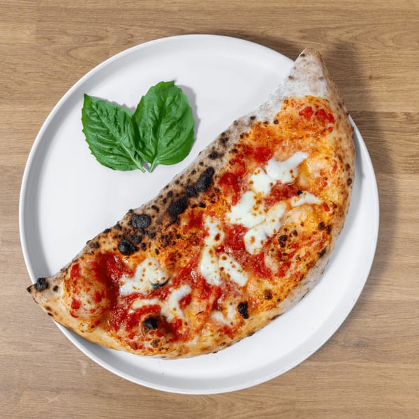A calzone with tomato sauce, melted mozzarella, and basil leaves on a white plate.
