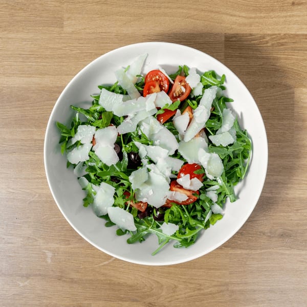 Arugula salad with cherry tomatoes, black olives, and shaved Parmesan cheese in a white bowl.