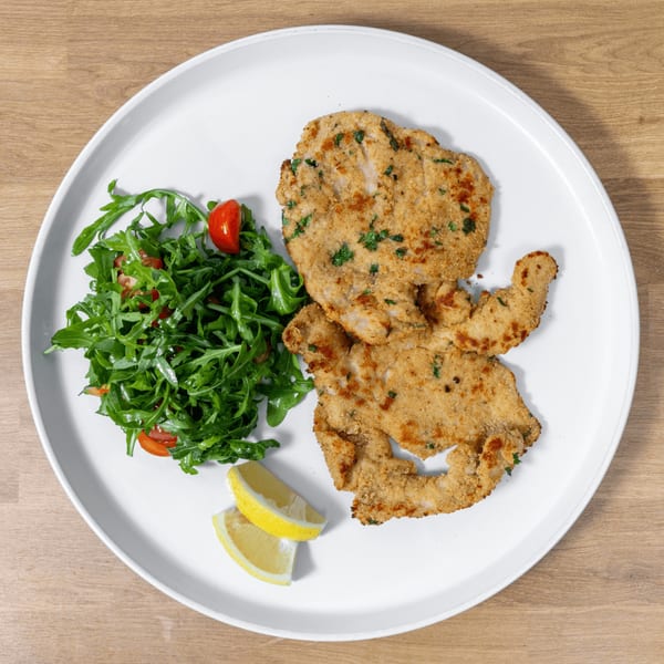 Crispy breaded chicken cutlets with a side of fresh arugula salad and lemon wedges on a white plate.