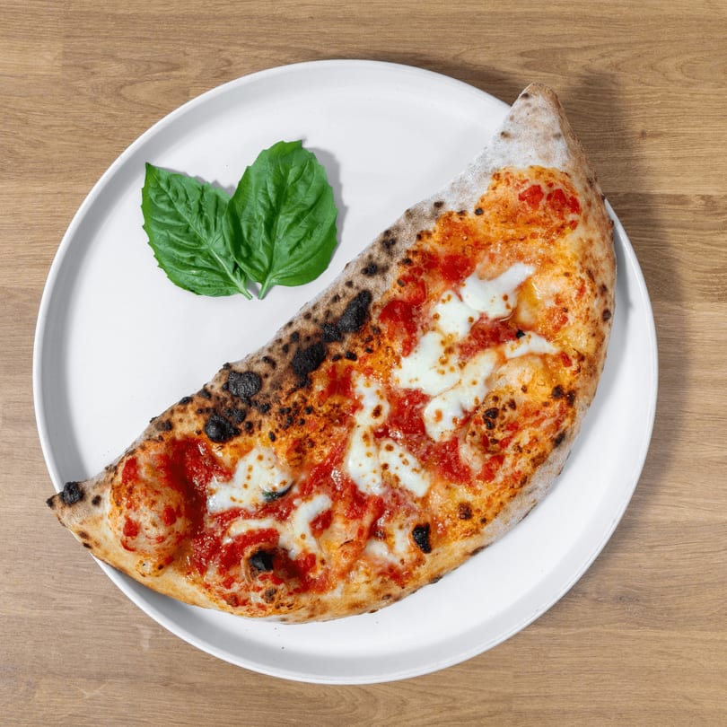 A calzone with tomato sauce, melted mozzarella, and basil leaves on a white plate.