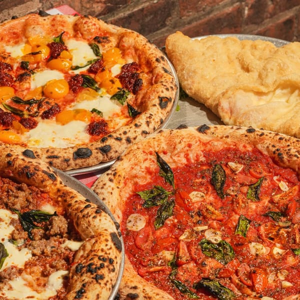 Three pizzas with various toppings and a fried calzone on metal trays.