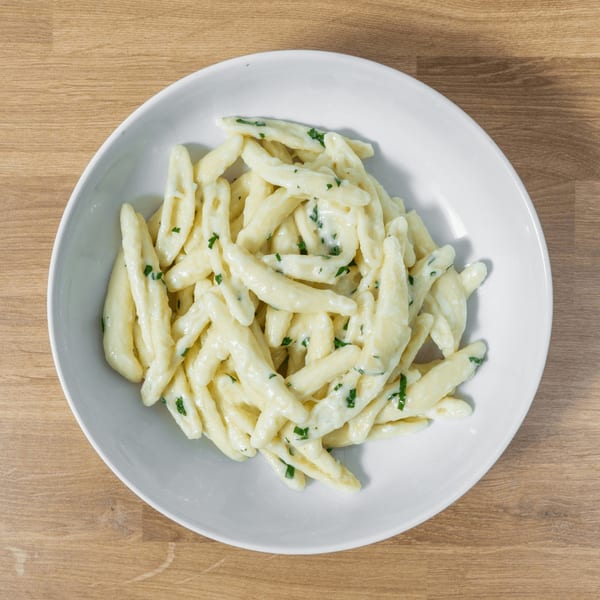 A white bowl filled with creamy, white cavatelli pasta and green herbs on a wooden table.