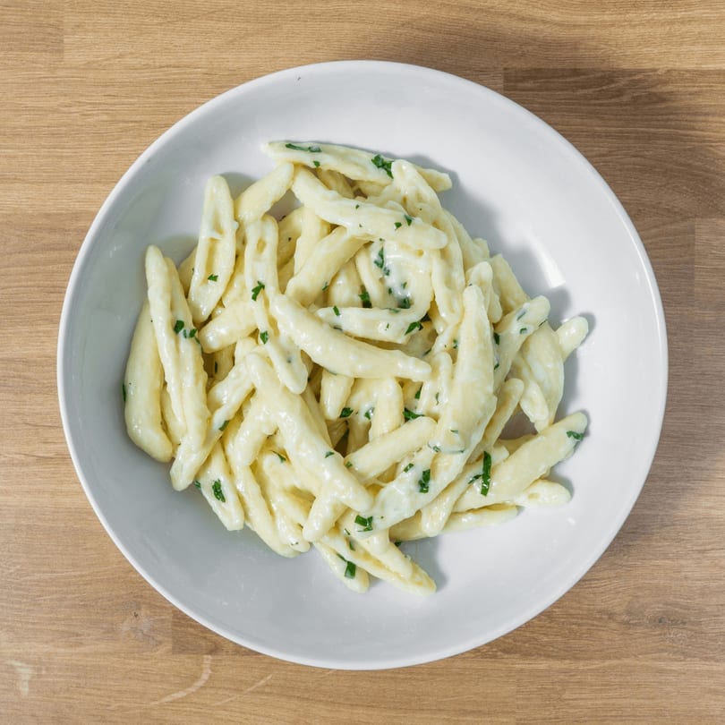 A white bowl filled with creamy, white cavatelli pasta and green herbs on a wooden table.