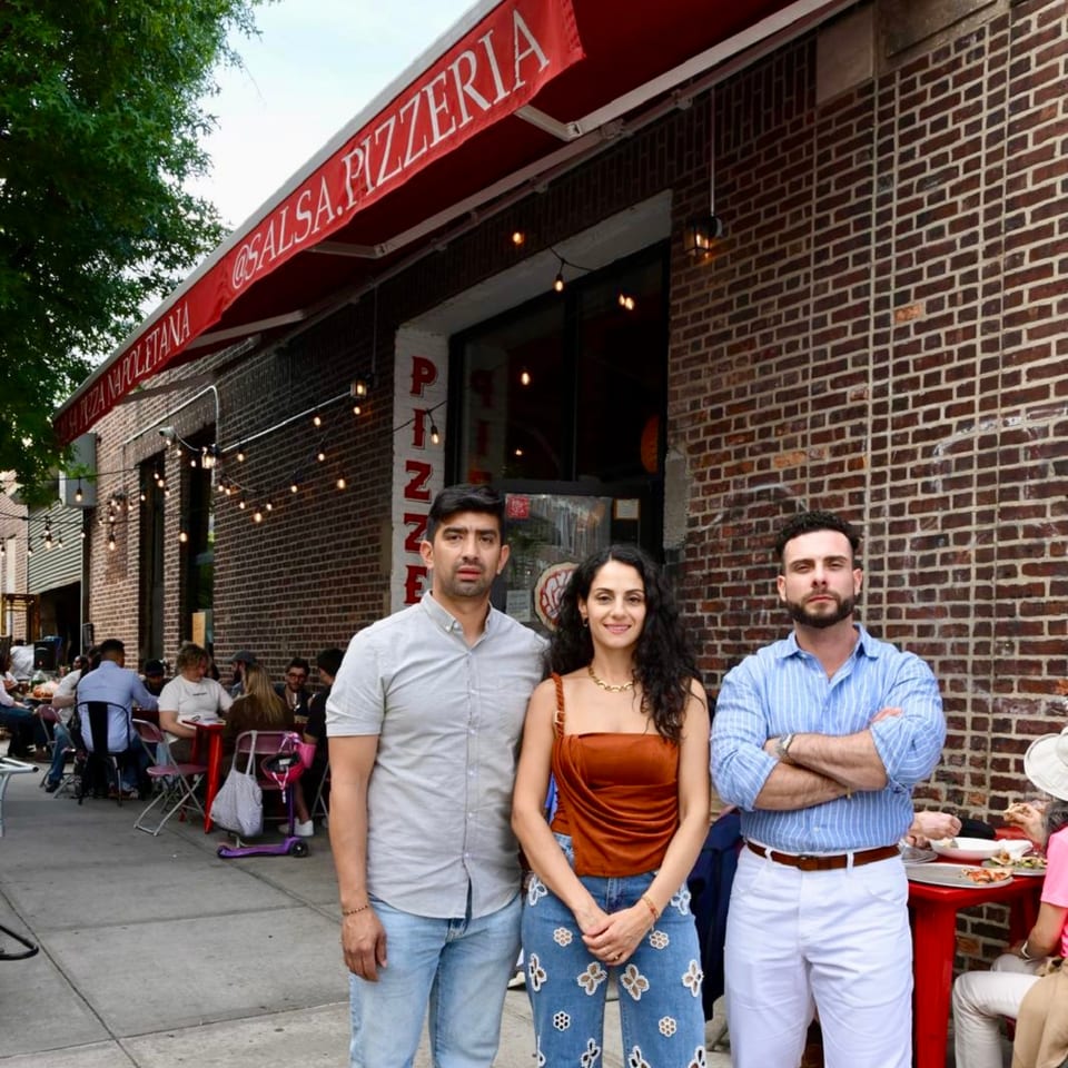 Three people standing in front of Salsa Pizzeria, with outdoor diners visible on the left.