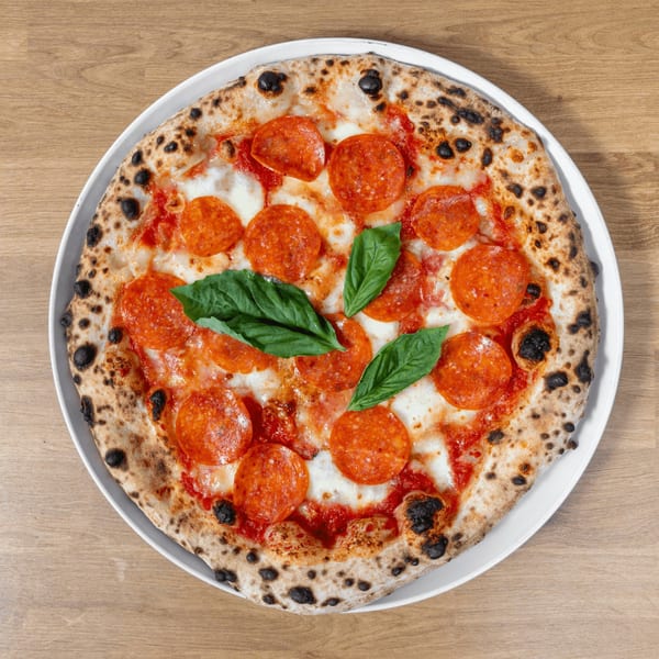 Overhead view of a pepperoni pizza with fresh basil on a white plate, on a wooden table.