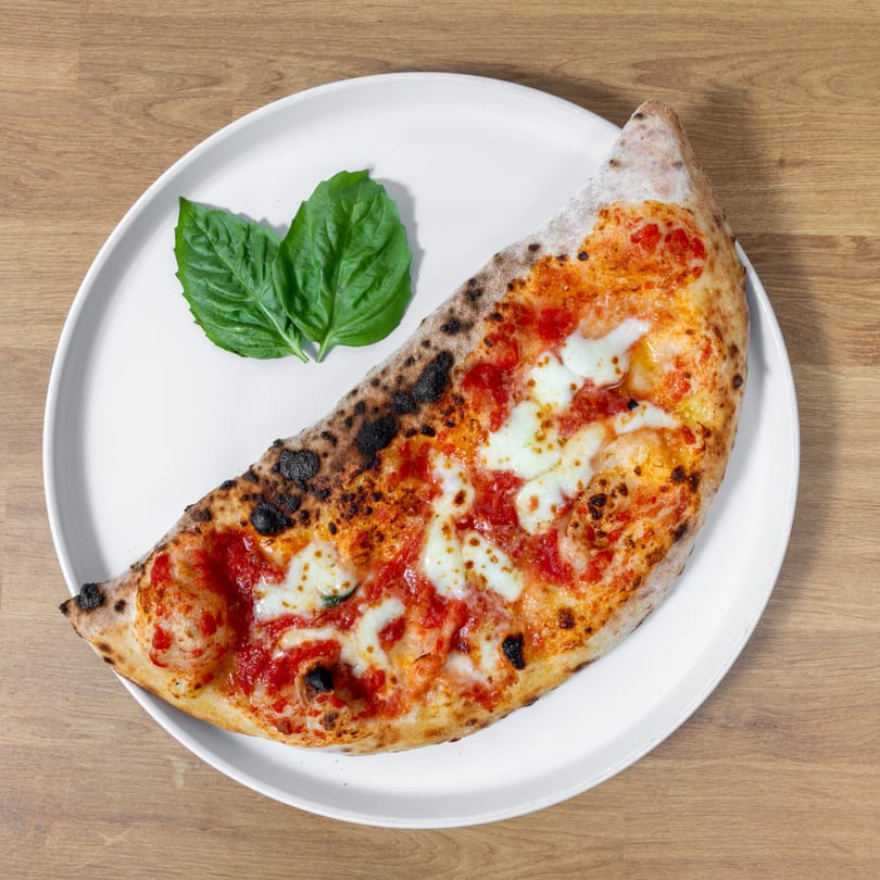 A half-moon calzone with melted mozzarella, red sauce, and basil on a white plate.