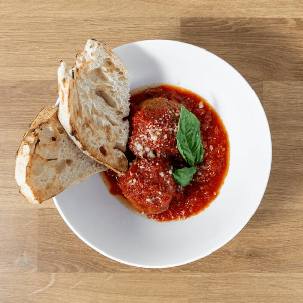 Meatballs in red sauce with grated cheese and basil, served with toasted bread on a white plate.