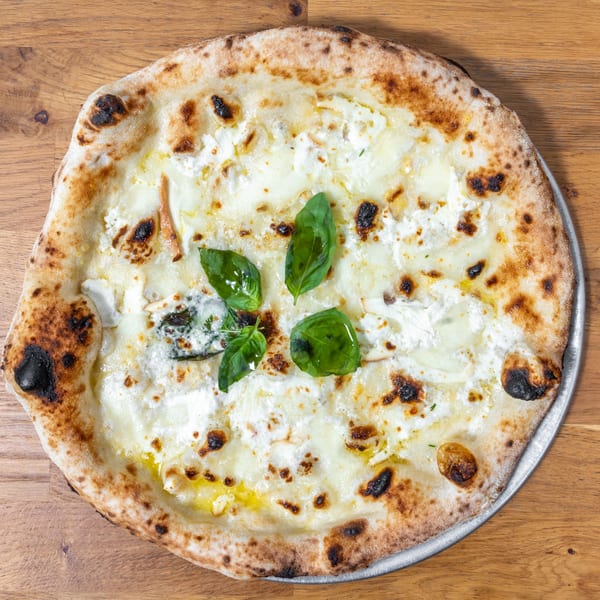 A white pizza with ricotta cheese, mushrooms, and fresh basil leaves on a wooden table.