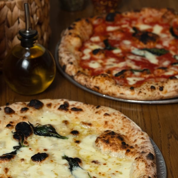 Two delicious Neapolitan pizzas, one white and one red, with an olive oil bottle on a wooden table.