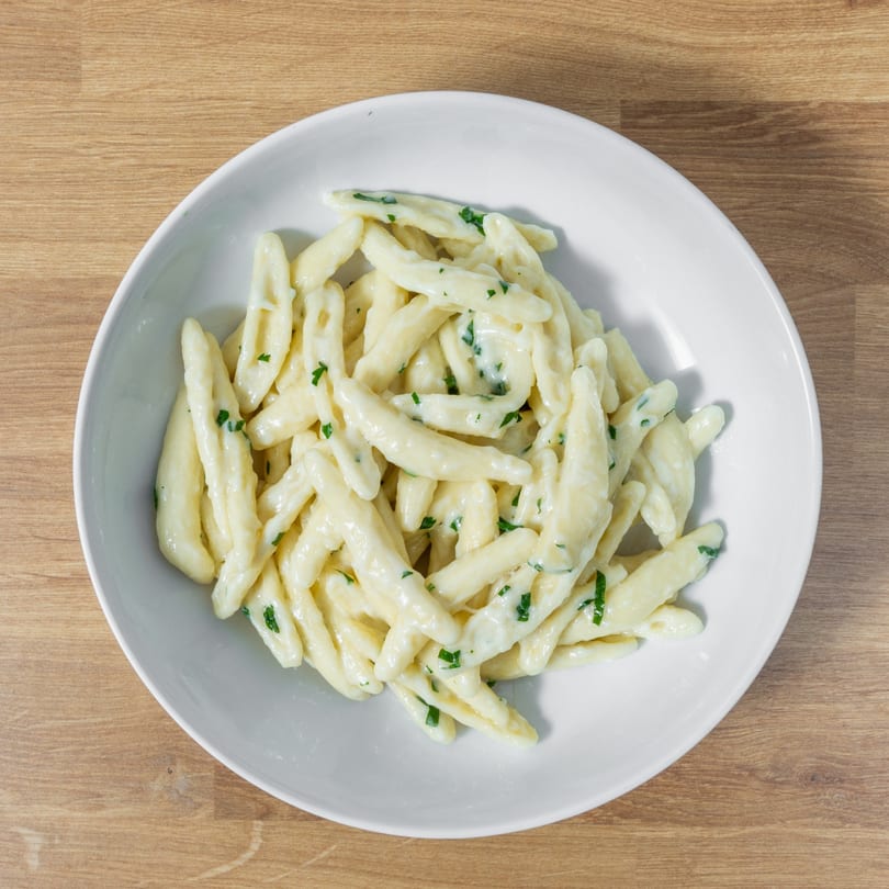 Top-down view of a white bowl filled with creamy pasta and green herbs on a wooden table.
