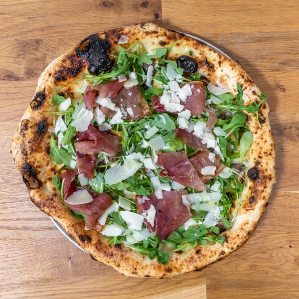 Neapolitan pizza with prosciutto, arugula, and shaved Parmesan on a wooden table.